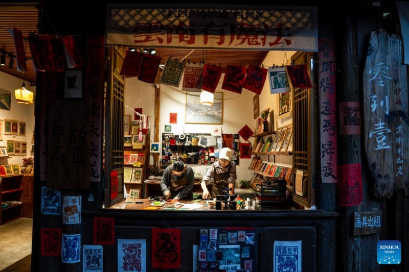 Ένας τουρίστας (αριστερά) δοκιμάζει να δημιουργήσει ένα τοπικό παραδοσιακό ξυλότυπο γνωστό ως Jiama στο χωριό Σιντένγκ της πόλης Σάσι, στην κομητεία Τζιεντσουάν, στη νοτιοδυτική Κίνα, στην επαρχία Γιουνάν, 18 Απριλίου 2025. 