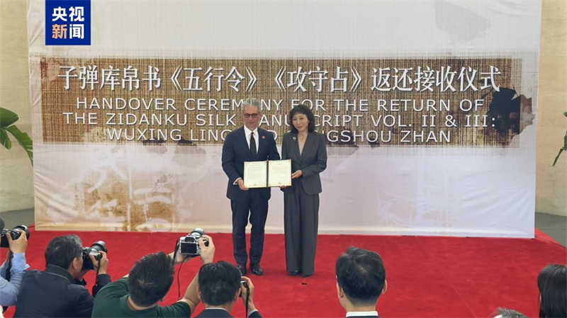 Η Τζου Γιέ (δεξιά), αναπληρώτρια γενική διευθύντρια του Γραφείου για την Ανάκτηση και Αποκατάσταση Χαμένων Πολιτιστικών Αγαθών, της Εθνικής Διοίκησης Πολιτιστικής Κληρονομιάς της Κίνας, λαμβάνει πιστοποιητικό μεταβίβασης από τον Τσέις Φ. Ρόμπινσον, διευθυντή του Εθνικού Μουσείου Ασιατικής Τέχνης του Σμιθσόνιαν, κατά τη διάρκεια τελετής παράδοσης των αρχαίων Χειρογράφων Μεταξιού Τζιντανκού από την περίοδο των Εμπόλεμων Κρατών στην Κινεζική Πρεσβεία στις Ηνωμένες Πολιτείες στην Ουάσινγκτον, στις 16 Μαΐου 2025. /CMG