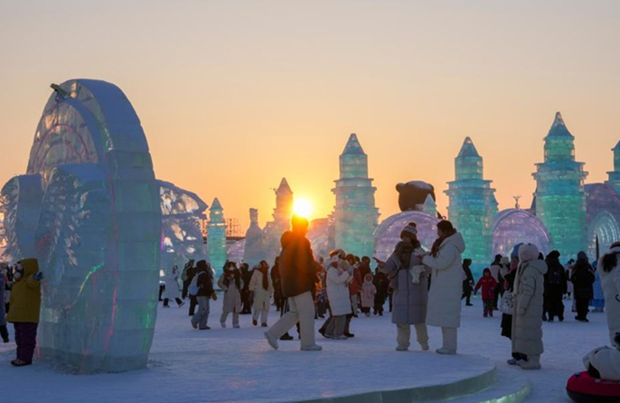 Οι τουρίστες διασκεδάζουν στο ηλιοβασίλεμα στον Κόσμο Πάγου και Χιονιού της πόλης Χαρμπίν
